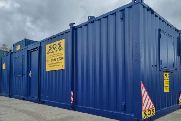 Dynamic 3/4 photo of a 32ft blue SOS cabin with yellow advertising board in clean yard surrounded by stacked containers and cabins.