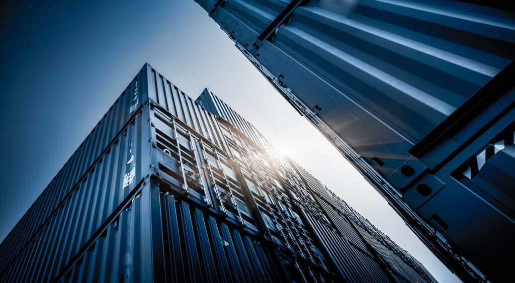 Stack of shipping containers viewed from ground level, showcasing their size and structure against the sky