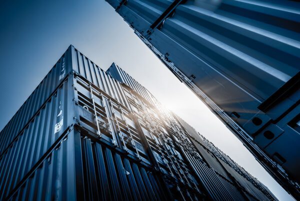 Stack of shipping containers viewed from ground level, showcasing their size and structure against the sky