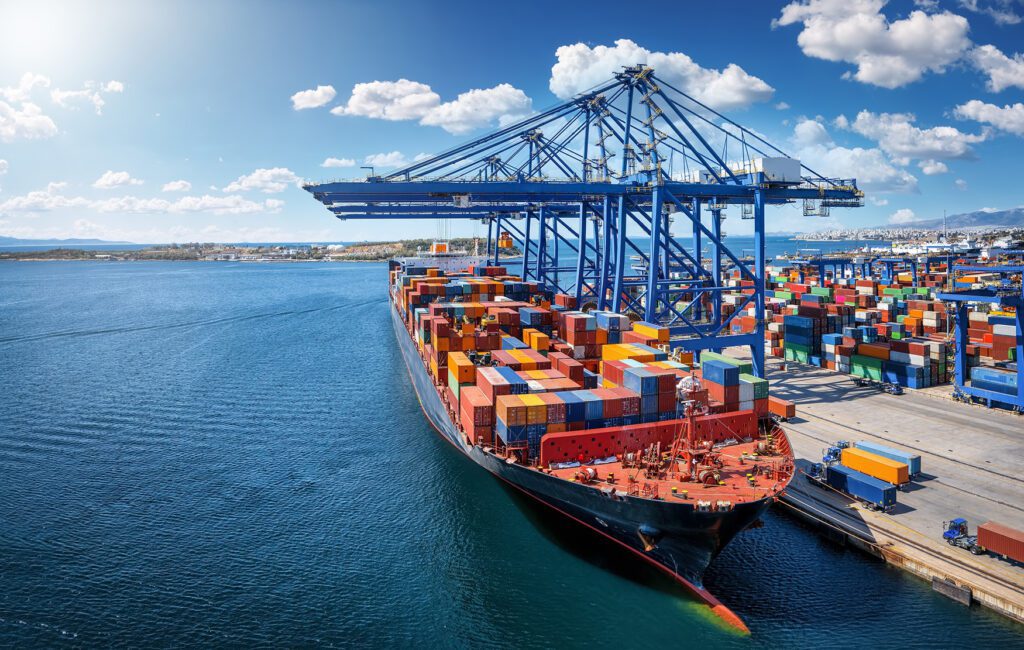 Large container ship docked at a port with colourful containers and cranes.