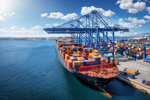 Large container ship docked at a port with colourful containers and cranes.