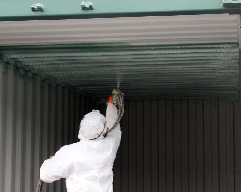 A worker applying spray foam insulation inside a shipping container.