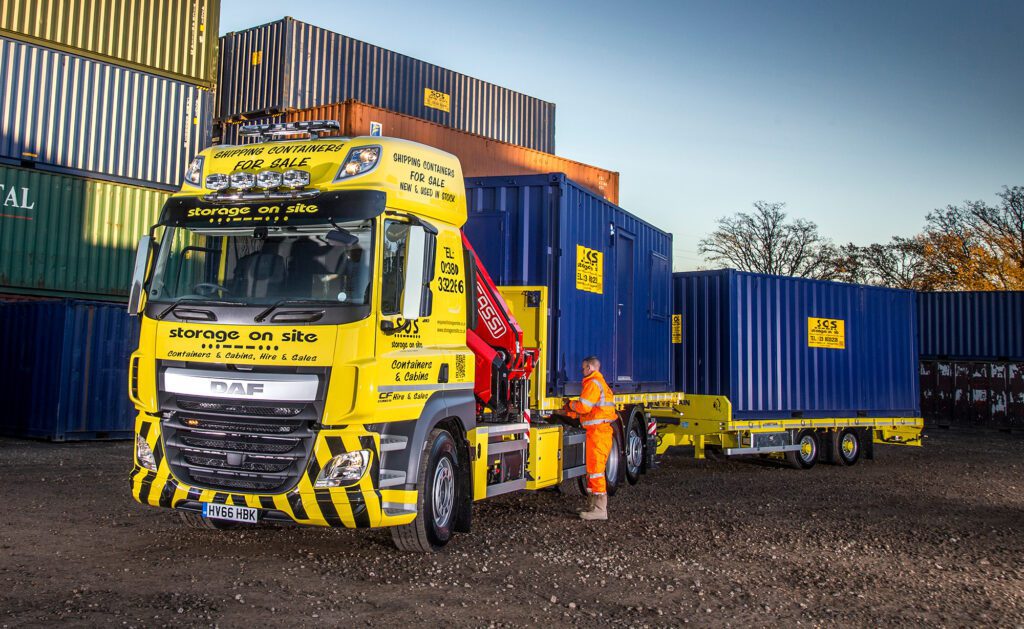 Crane-assisted HGV lorry delivering a storage container to a site.